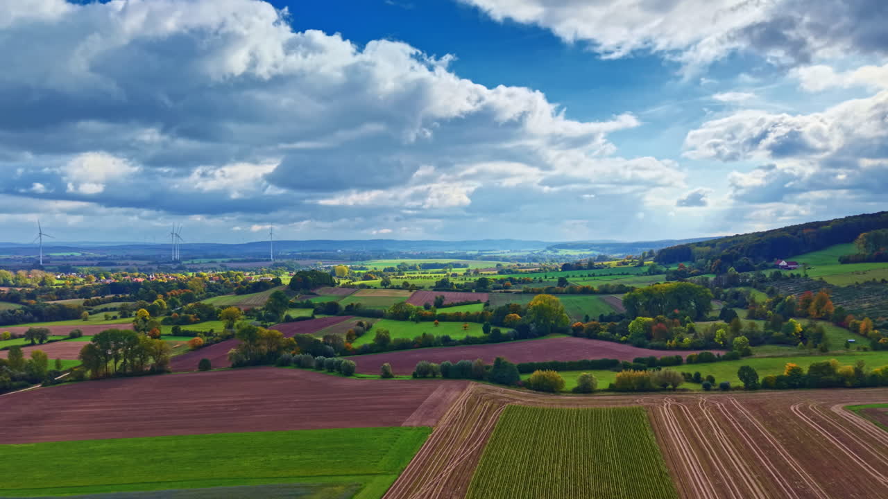 Vibrant countryside landscape showcasing lush fields and rolling hills under a bright sky filled with fluffy clouds during early autumn afternoon