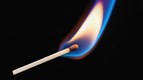 A burning matchstick with a bright flame against a dark background