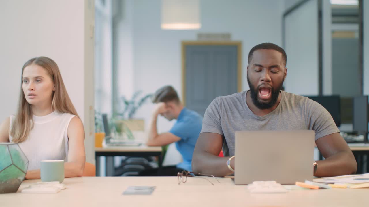 Black man yawning at workplace. Tired man supporting head sitting near notebook.