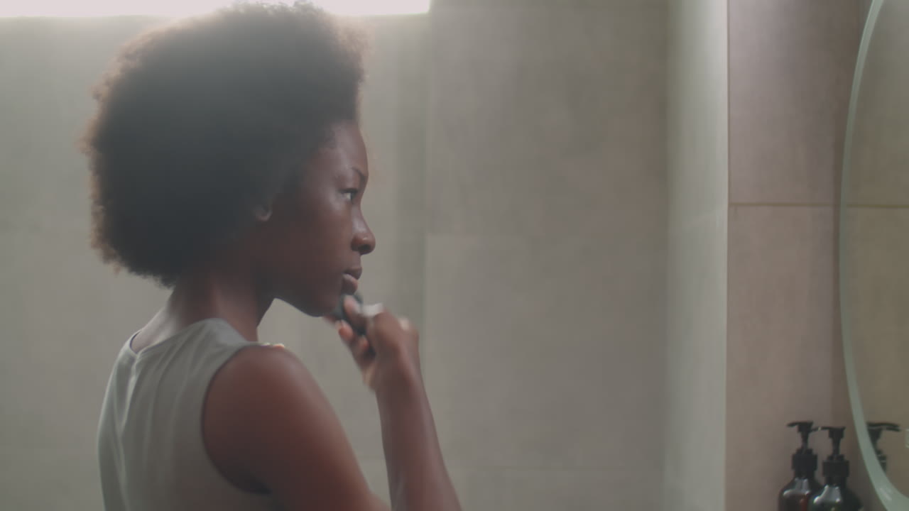 African American Woman Brushing Hair in Bathroom