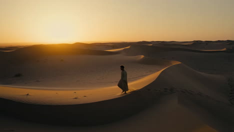 a man walking in the desert at sunset