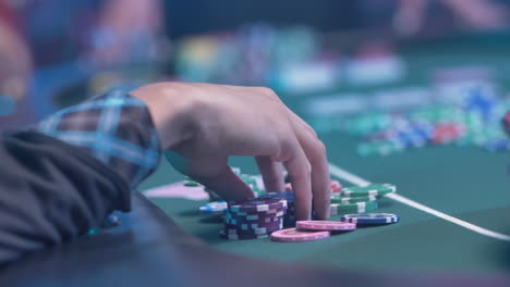 unidentified person's hand holding colorful chips on green table with defocused background inside the casino