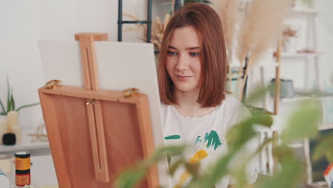 a red haired young female artist painting a canvas