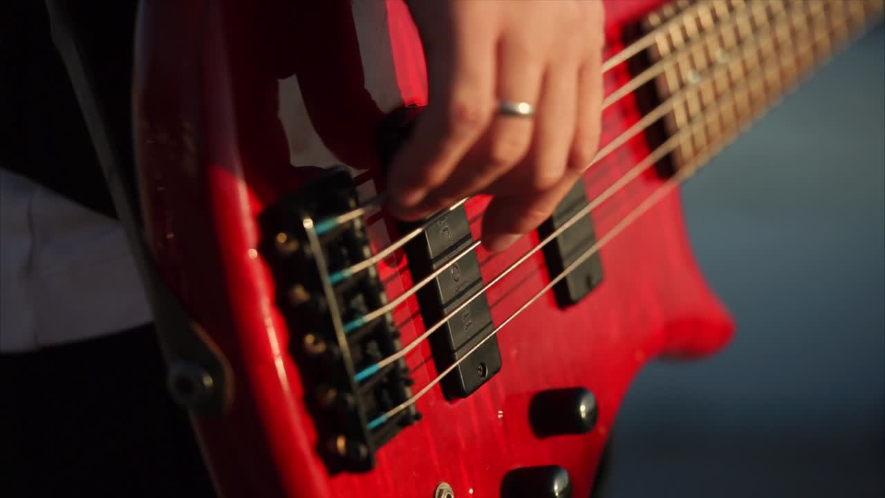 Close-up of hands playing a red bass guitar