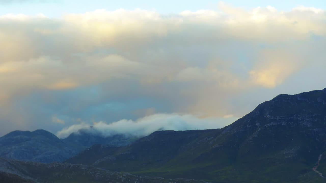 Time lapse of a mountain range with low fast moving clouds beneath high puffy clouds in the evening in the  Western Cape of South Africa.