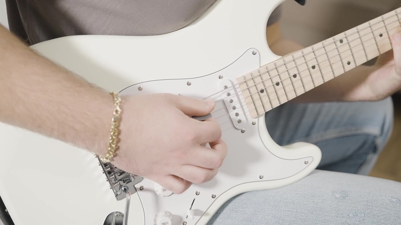 Beyaz bir elektro gitar çalan genç bir adamın yakın çekimi.