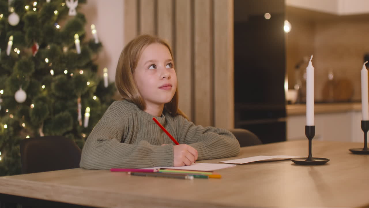 девушка в зеленом свитере пишет письмо и думает о желаниях, сидя за столом в комнате, украшенной рождественской елкой 2