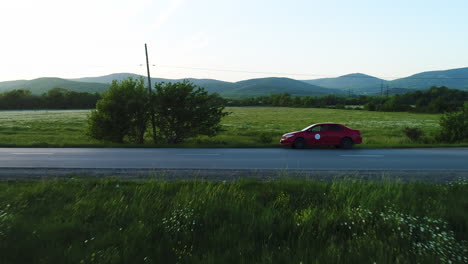 red car on a country road with mountains and fields