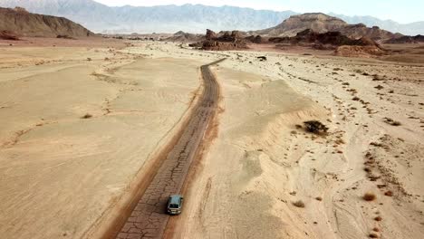 Coche-De-Pasajeros-Conduciendo-Suavemente-Por-El-Camino-De-Tierra-Seco-Roto-Entre-El-Cañón-Rojo-En-El-Parque-Seco-De-Timna-En-El-Desierto-De-Negev-En-El-Sur-De-Israel-En-Un-Día-Soleado