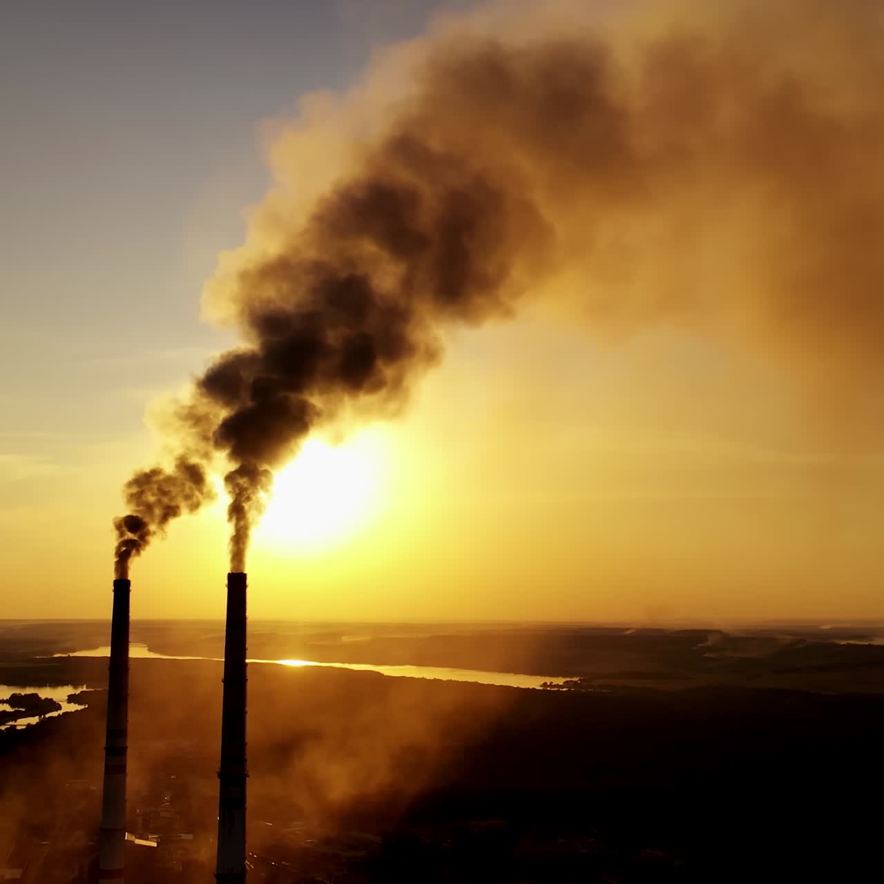 Dirty emissions in nature at sunset. Thick smoke coming from industrial pipes on the yellow sun setting background. Ecological disaster.