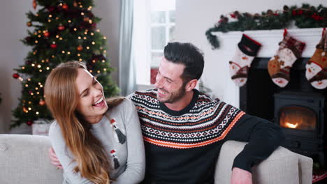 Retrato-De-Una-Pareja-Vistiendo-Puentes-Festivos-Sentados-En-Un-Sofá-En-El-Salón-De-Casa-El-Día-De-Navidad