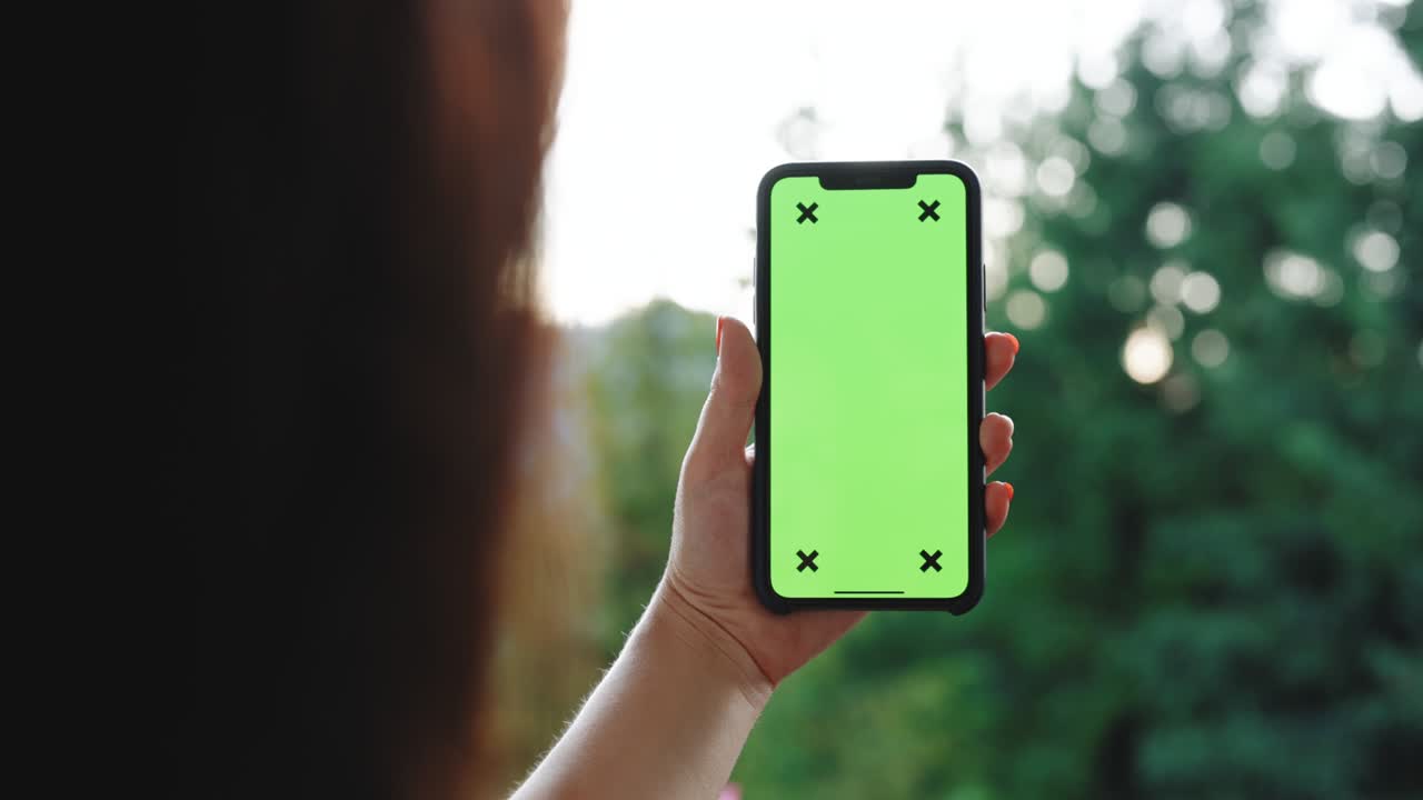 Back View of Woman Holding Chroma Key Green Screen Smartphone Watching Content Without Touching or Swiping. Girl Using Mobile Phone, Browsing Internet, Watching Content