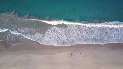 top down aerial, waves breaking on the sandy shore of shoal bay in australia, people walking on beach during golden hour