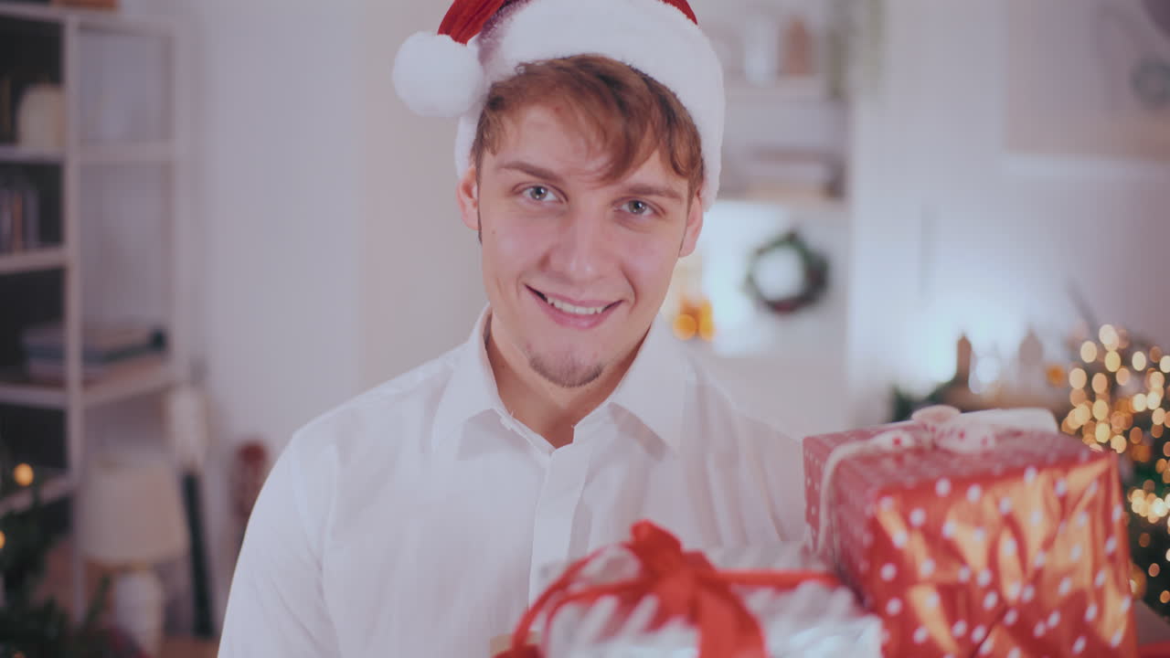 예쁜 남자가 집에서 크리스마스 선물을 보면서 미소 짓고 있다