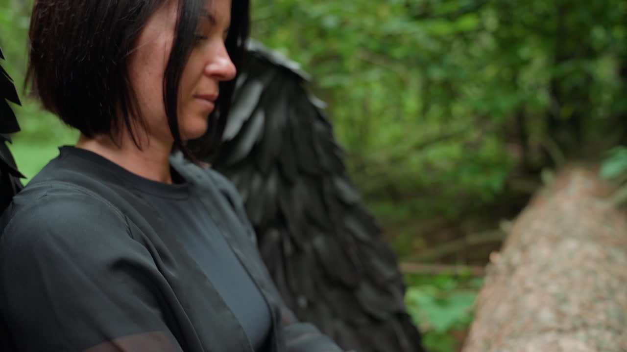 Black fairy with sheer black sleeves plucking metal tines on small green kalimba resting on fallen trunk in lush forest, soft light highlighting serene motion