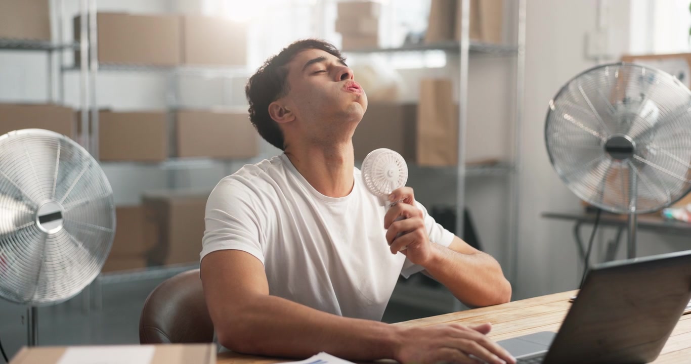 Jovem usando ventilador de mão para se refrescar enquanto trabalha na mesa