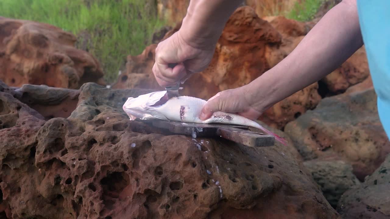 preparación de la cocina costera: las manos del hombre limpian los huesos de pescado en la orilla del mar