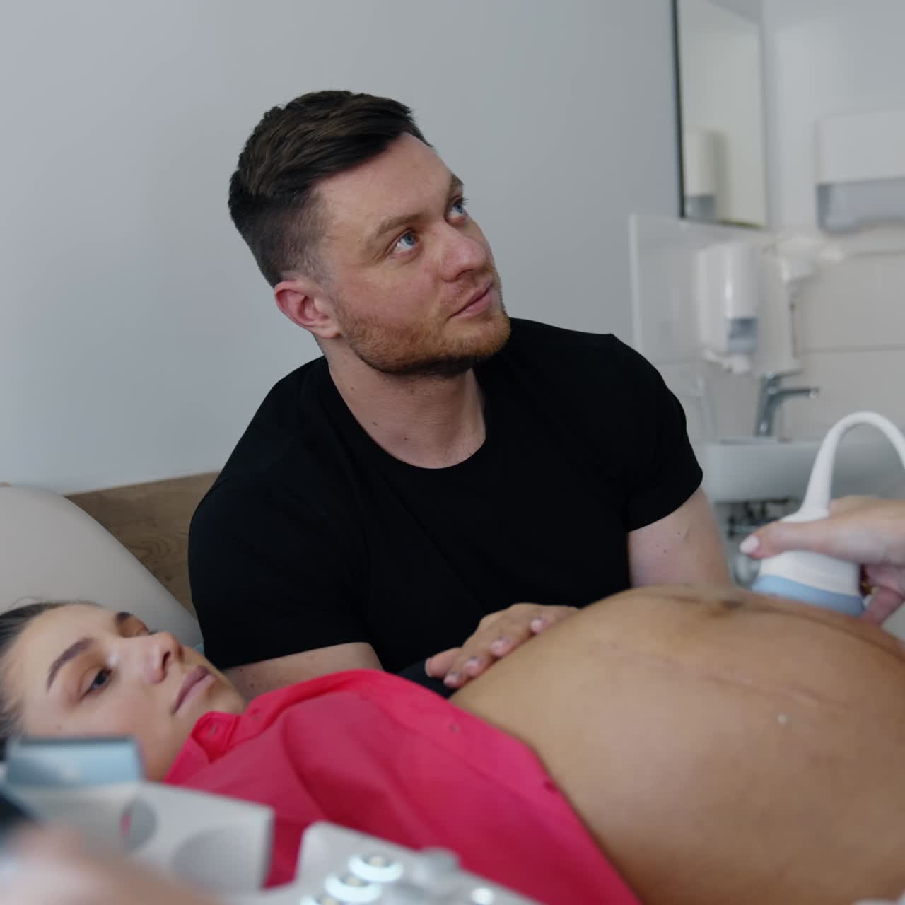 Future parents attentively look on the screen in doctor's cabinet. Caucasian couple is on the ultrasound pregnancy check up