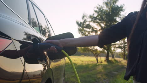 woman plugging in the charger in an electric car, going for walk, handheld shot