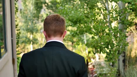 shot from behind an androgynous queer person as they walk down stone steps of a mansion to their backyard wedding