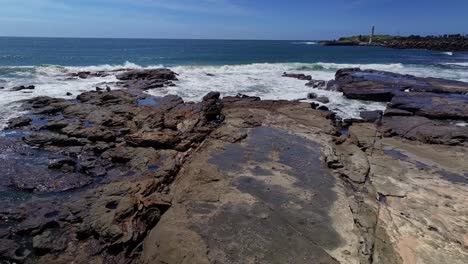 aérea sobre las rocas y las olas que se estrellan hacia los faros en el puerto de wollongong