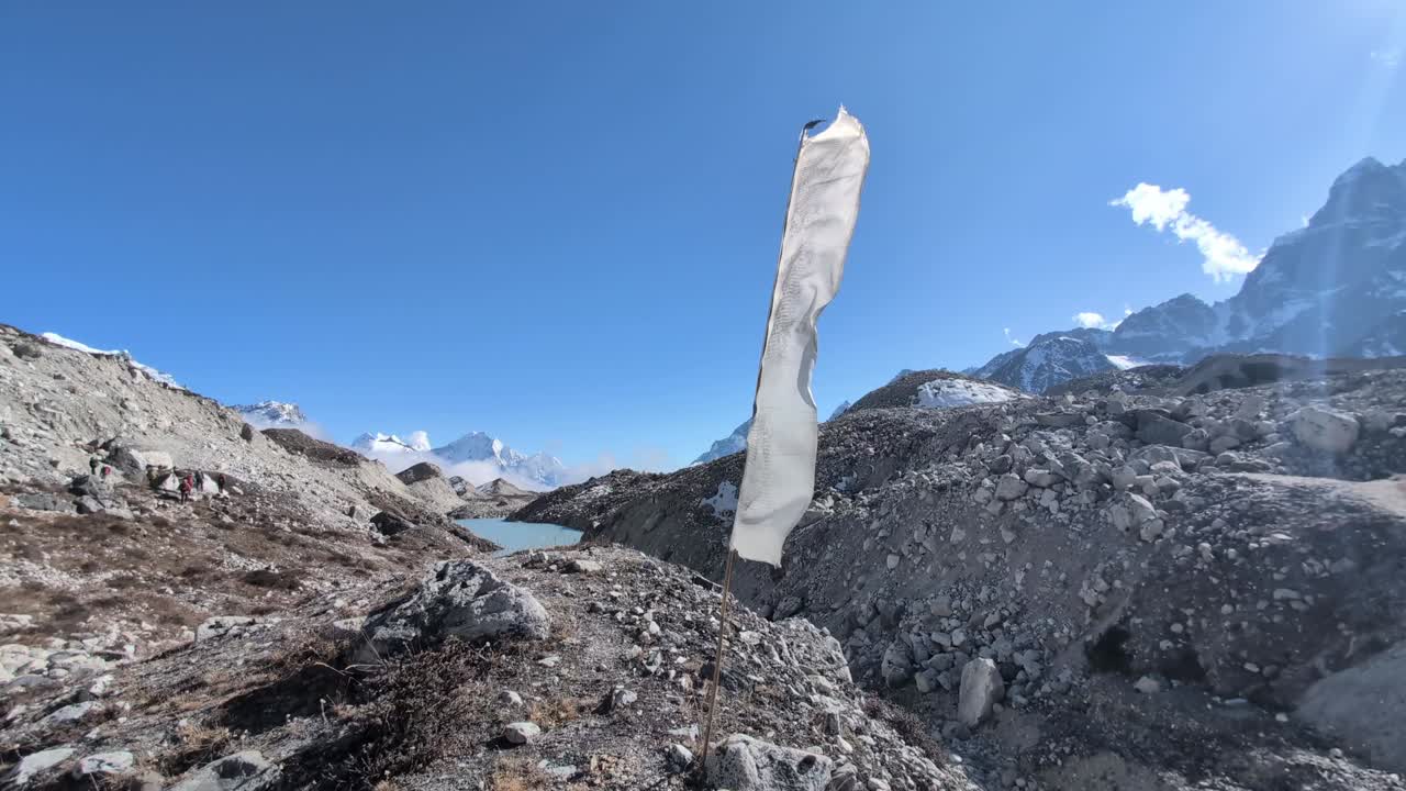 una bandera de oración blanca ondea en el fuerte viento en lo alto de un asta de bandera plantada en el vasto glaciar ngozumba, un símbolo de espiritualidad y resiliencia en medio de la dura belleza de los himalayas.
