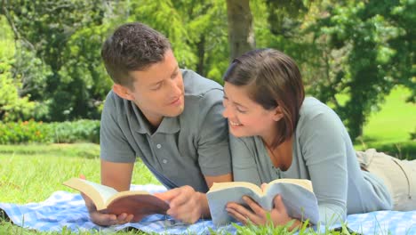 pareja joven leyendo un libro mientras se acuesta en el césped