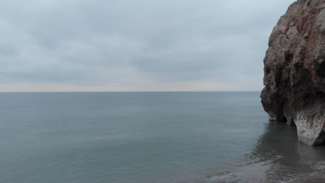 drone-flies-at-a-low-altitude-past-cliffs-and-out-over-serene-glassy-surface-of-calm-sea