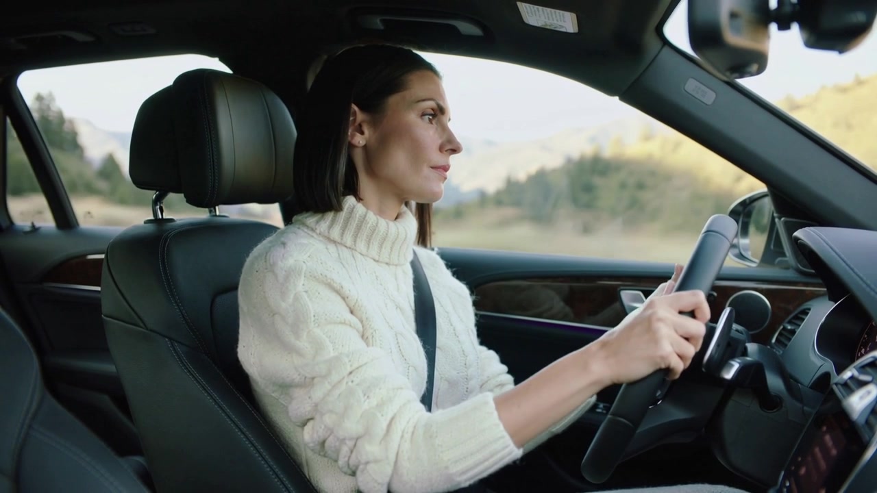 Strada rurale tortuosa, una donna alla guida con maglione di maglia bianco e cintura di sicurezza che aggiusta il volante in auto.