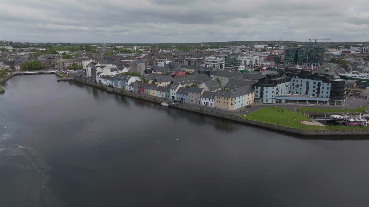 Una toma cinematográfica con dron que captura las coloridas casas de Long Walk y el tranquilo río Corrib en Galway, Irlanda, bajo un cielo nublado.