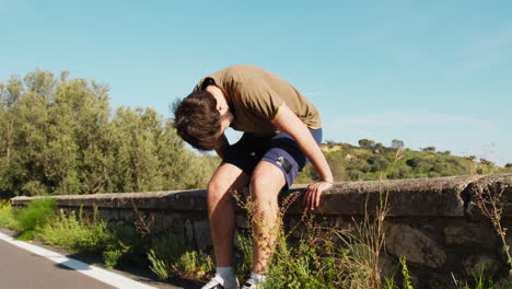 very tired athlete stops to rest on a low wall by the road
