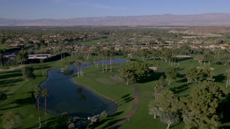 aerial view of a lush golf course with water features and palm trees set against desert mountains and residential areas