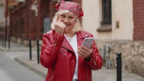 senior woman use mobile smartphone celebrating win good message news outdoors in urban city street