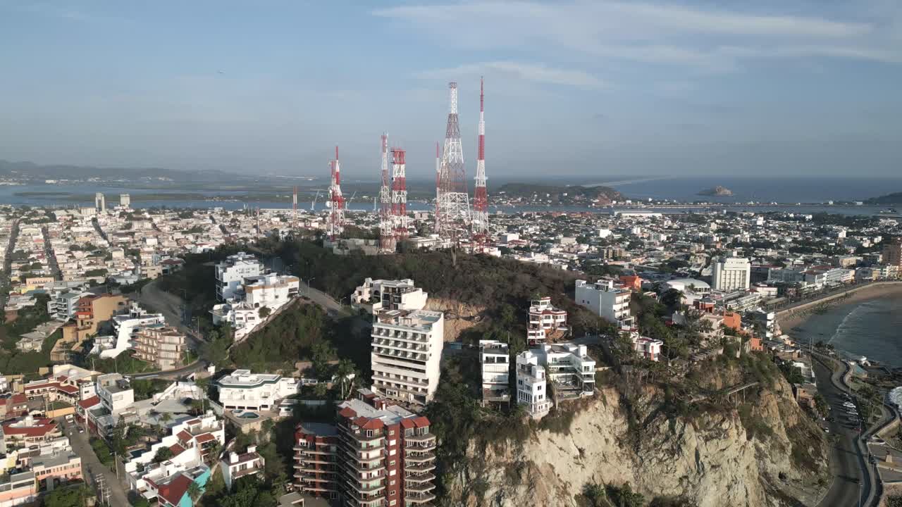 멕시코 마자틀란의 태평양 해변 의 절벽에서 드론이 날아다니며 파도가 해안 도시, 바다 및 5g 통신 타워를 따라 스카이라인을 부수고 있습니다.