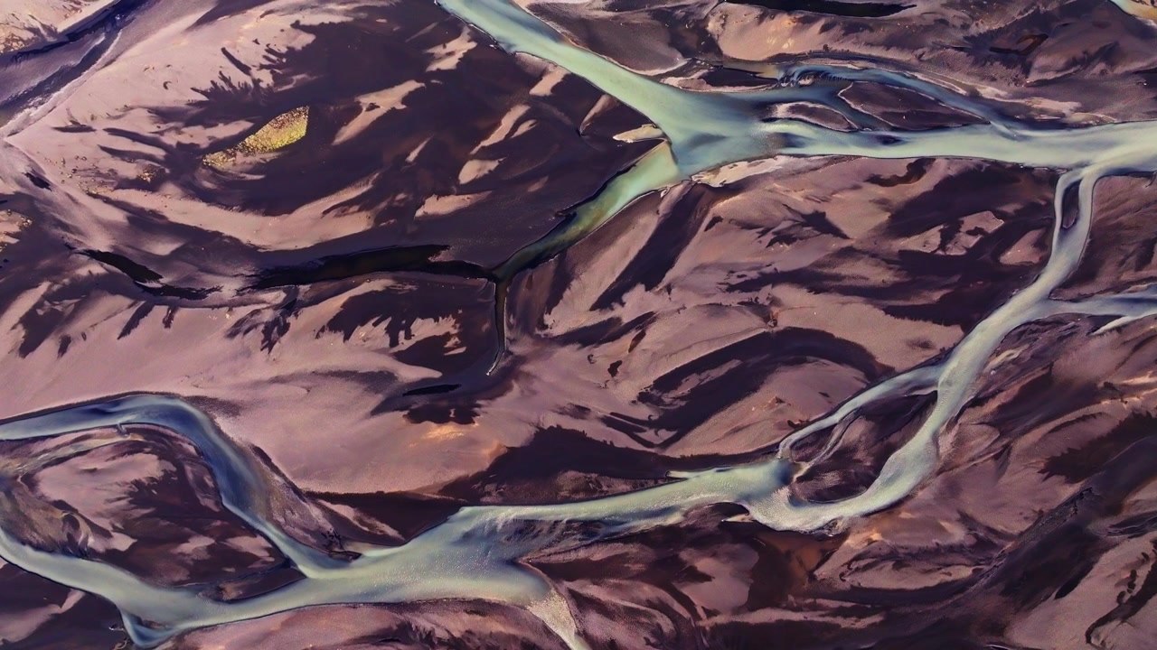 A mesmerizing top-down aerial view of a braided river in Iceland. Milky glacial meltwater weaves intricate, vein-like patterns through dark volcanic sand, highlighting the raw beauty of the Icelandic
