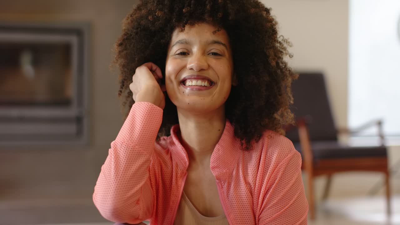 Donna afroamericana che ruota la testa e sistema un ricciolo mentre è seduta al tavolo, sorridendo e guardando in camera
