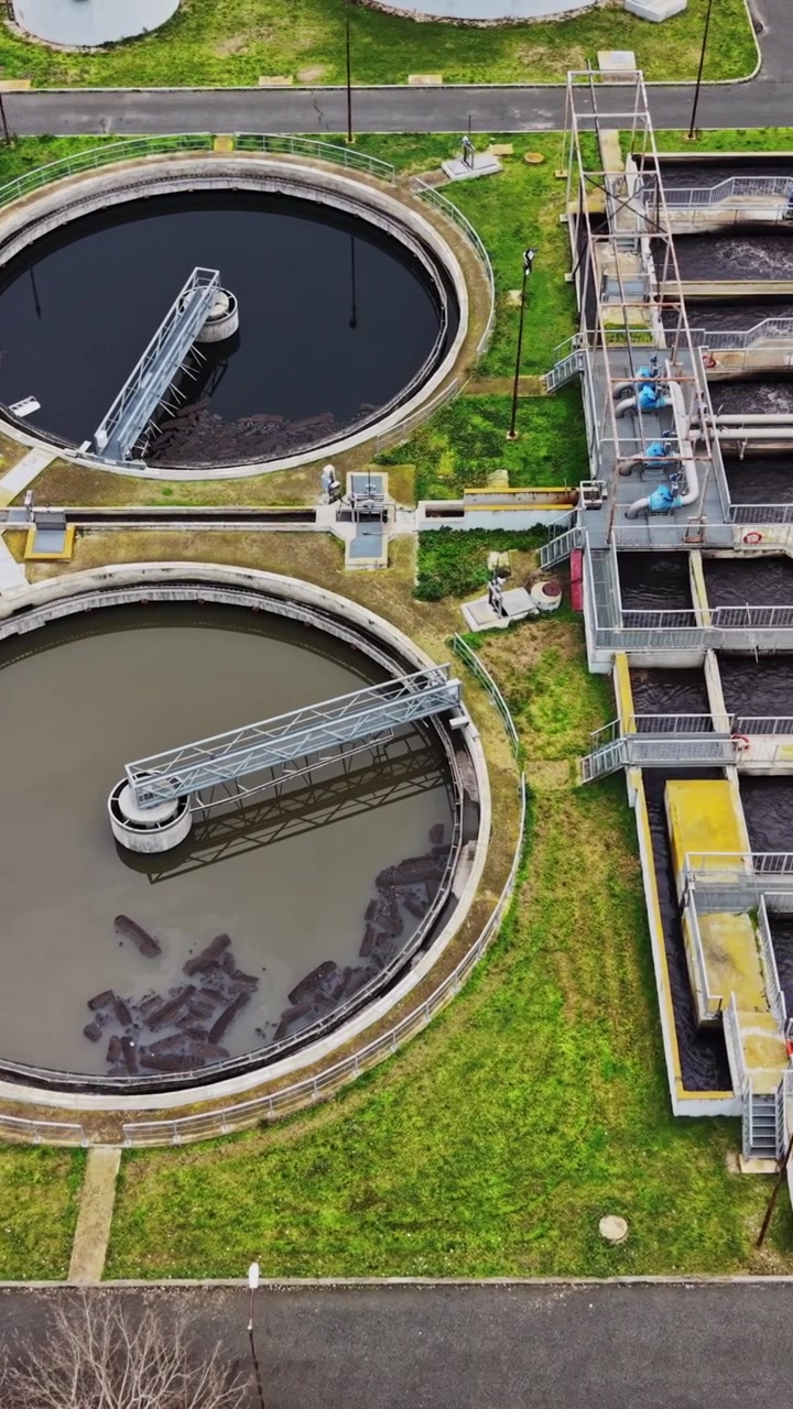 Workers manage a wastewater treatment facility with tanks and buildings