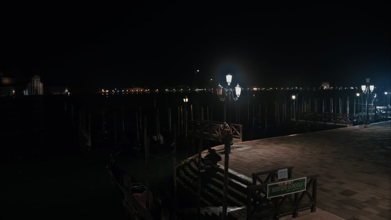 Ormeggio di gondole a Venezia di notte con le luci della città sullo sfondo