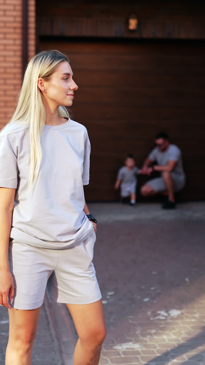 Family moment captured outside a home. A woman stands confidently by her home as a child and man enjoy a casual family day in the background