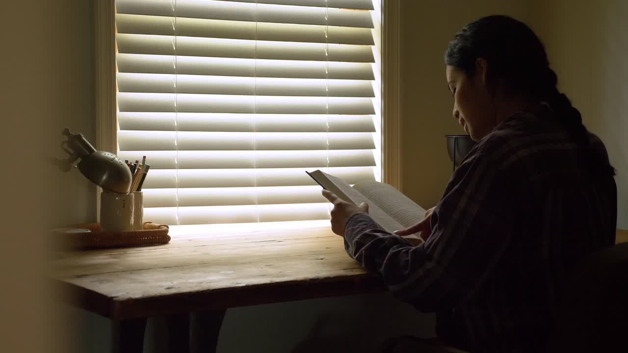 침실 창문 조명에 의한 책상에서 지적 책을 읽고 앉아있는 푸에르토리코 여성의 뒷면