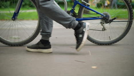 close-up of someone's legs walking beside a bicycle along a park walkway, the focus is on the legs and bike, with shoelaces in motion, the background is blurred, showing people walking