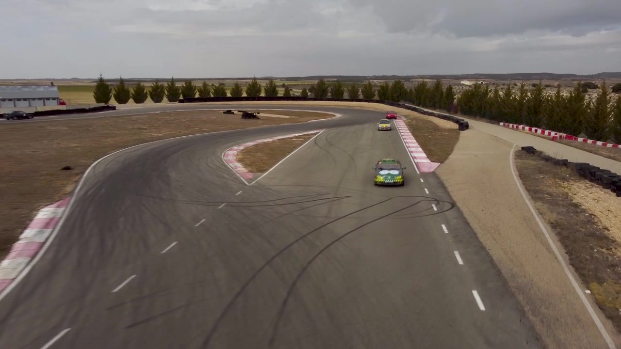 En dynamisk droneoptagelse af racerbiler, der bevæger sig mod kameraet på en racerbane.