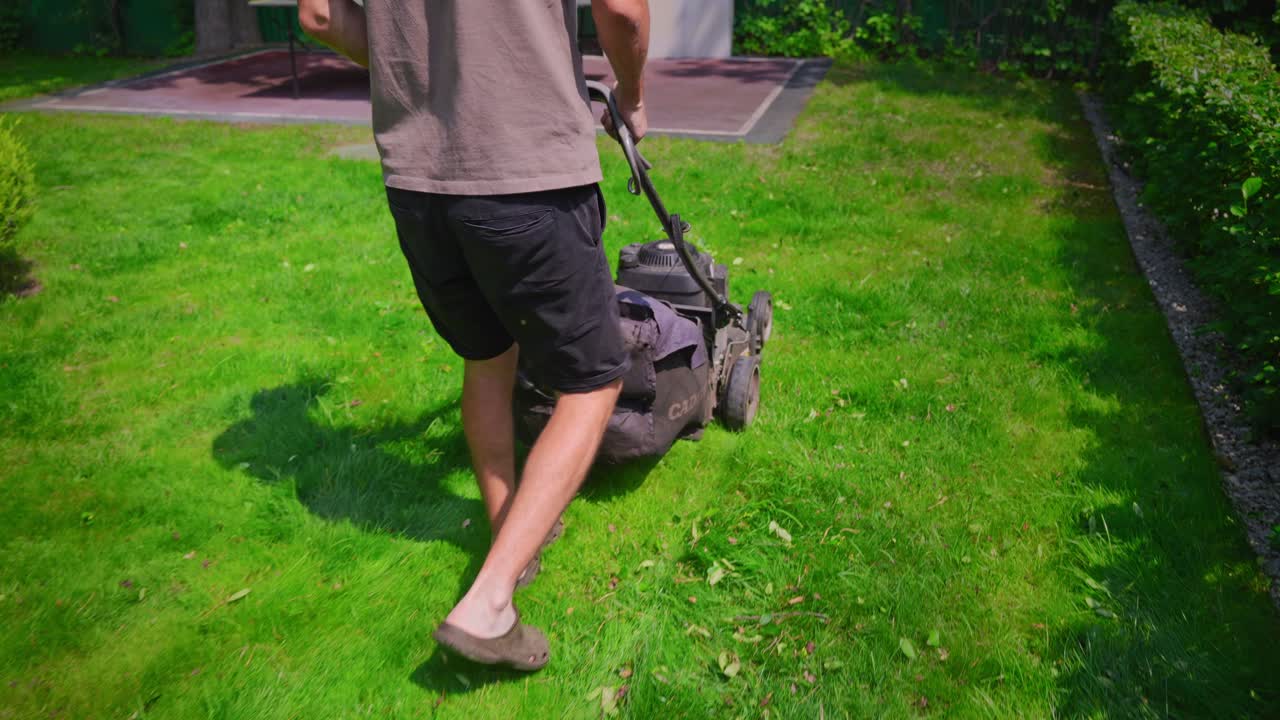 Man Mowing Green Grass Lawn in Backyard on a Sunny Day