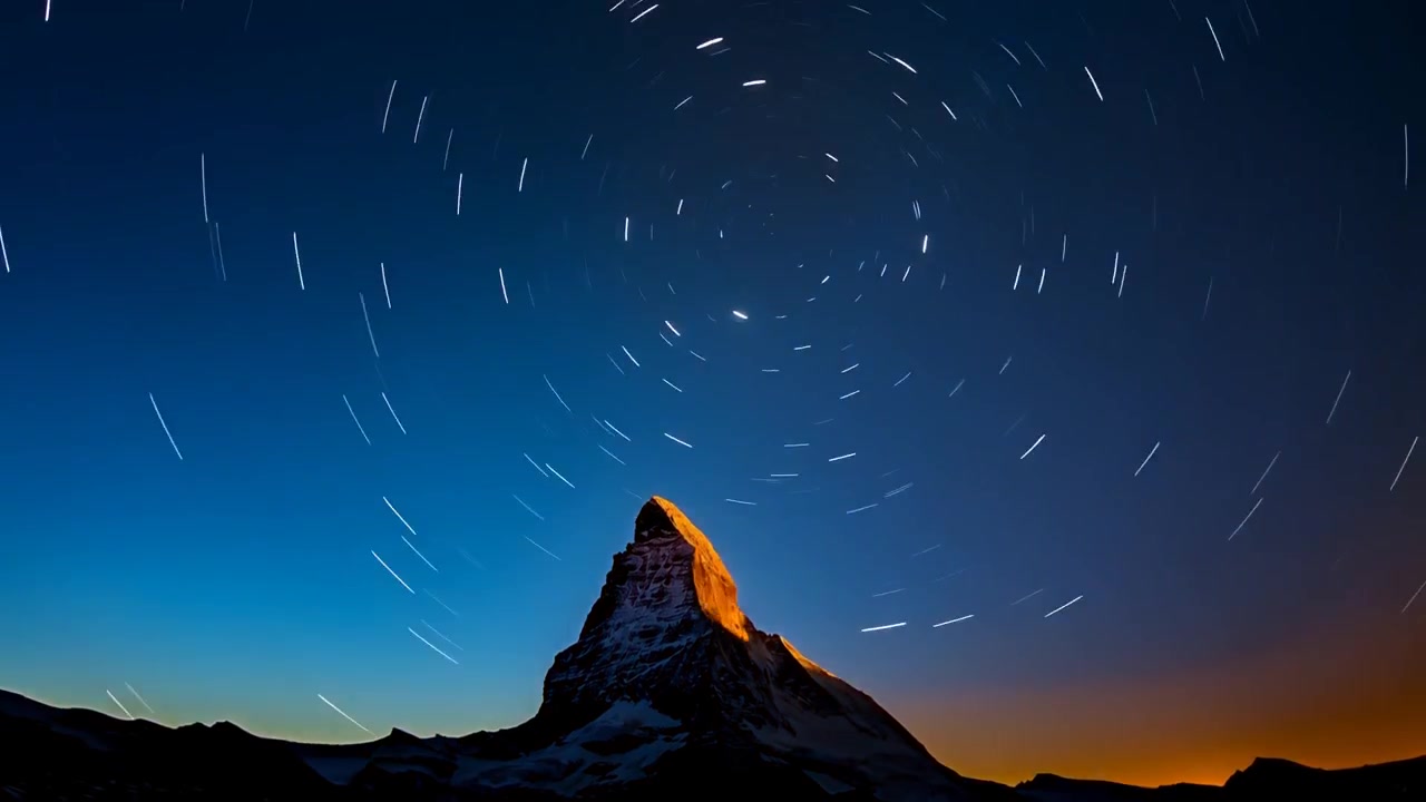Cámara de lapso de tiempo comenzando al resplandor del horizonte filmando rastros de estrellas rodeando una pirámide nevada hacia el amanecer