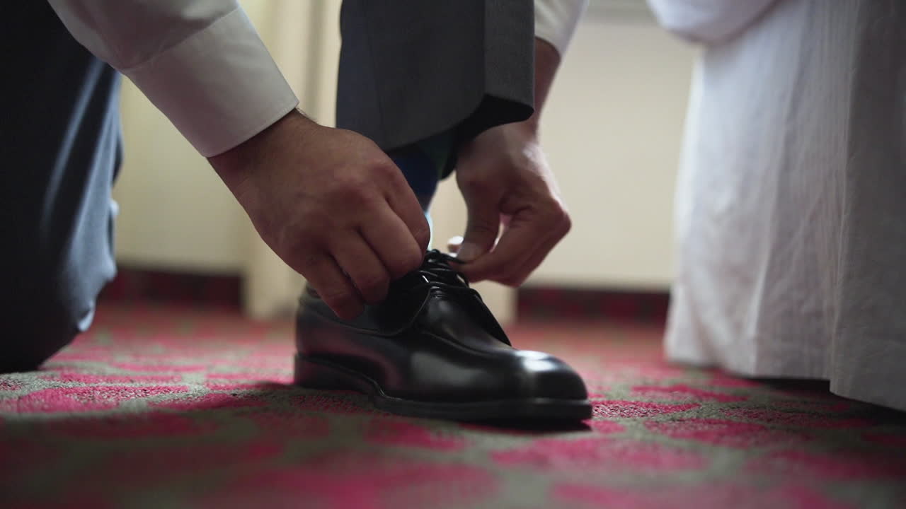 Groom tying his shoe lasses in a hotel room on his wedding day