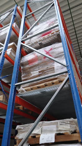 high metal shelves of blue color are filled with wooden boards in the building of a warehouse of a woodworking factory. view of the large storage of parquet from inside vertical video
