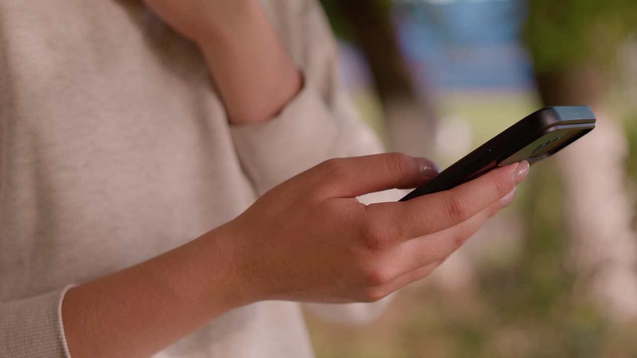 primer plano de la mano del individuo deslizándose sobre la pantalla del teléfono inteligente, involucrado en la interacción, el fondo natural al aire libre está suavemente borroso, mientras que los toques de vegetación y una figura indistinta en la distancia