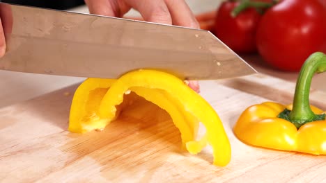 manos cortando pimientos amarillos en una tabla de madera