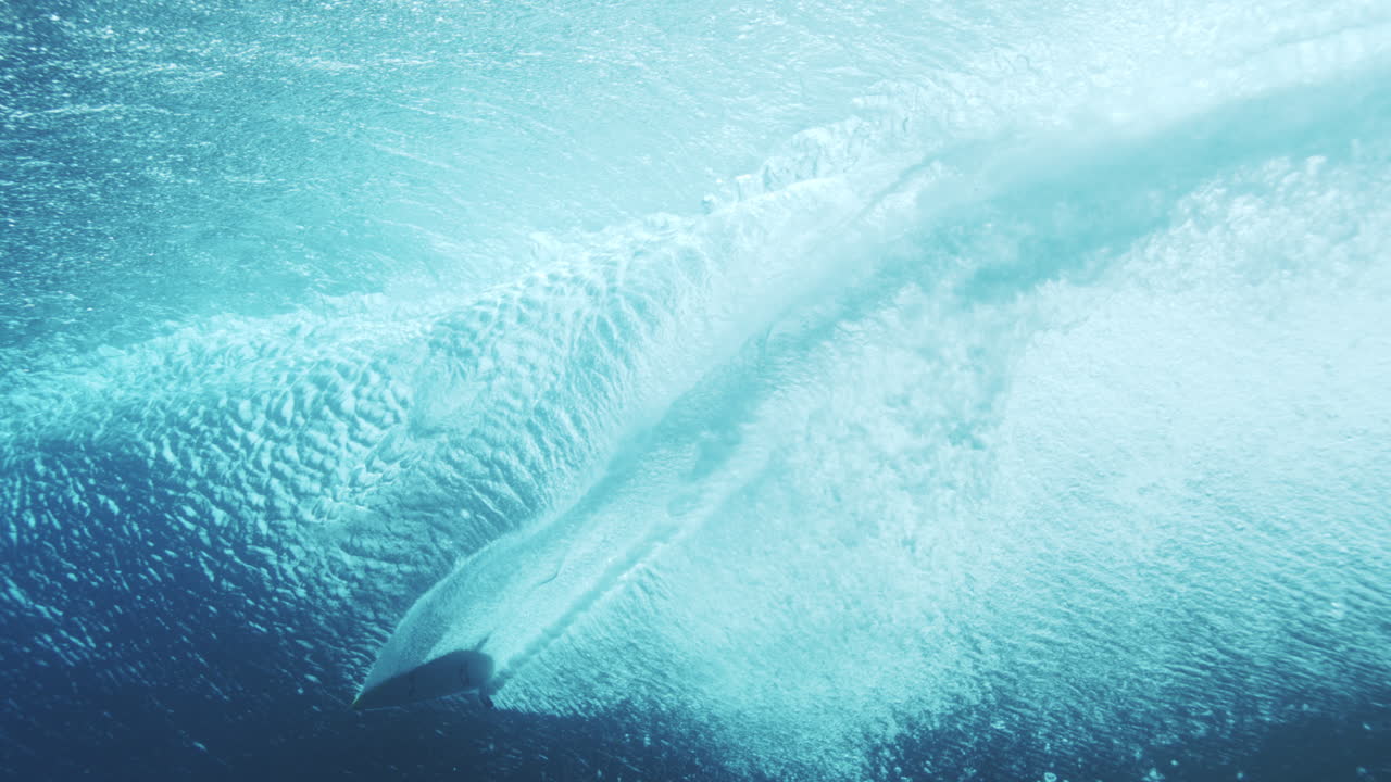 Dreamy white wash erupts from backside of wave as surfer drags hand through barrel, underwater rearview pov