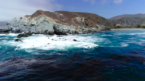 Aerial-Wraparound-of-Ocean-Waves-Sweep-Over-Large-Rocks-in-Water-off-of-the-Island